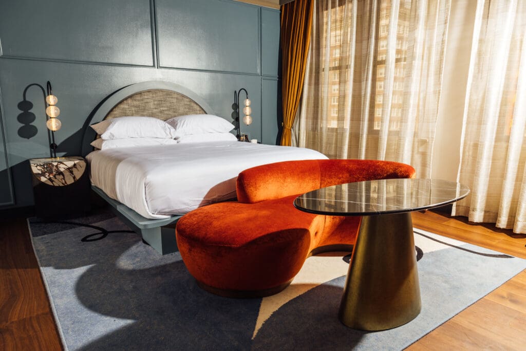 A modern king bed suite at The Gunter Hotel with elevated finishes and furnishings, bed bedside table and a fainting couch and table.