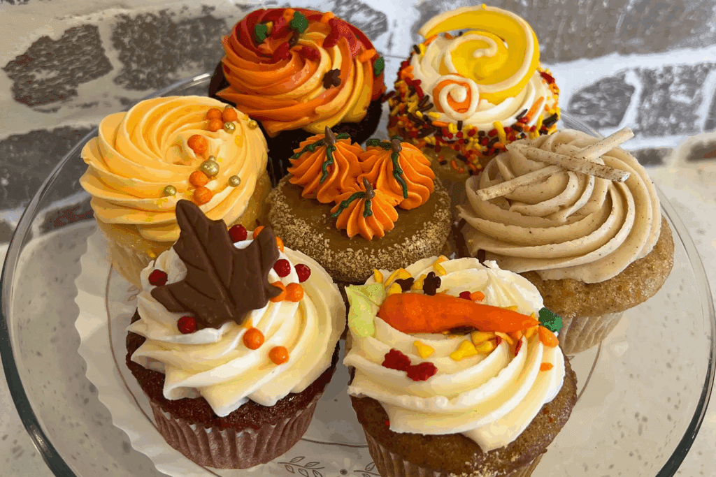A plate of six decorative fall-themed cupcakes with autumn leaves, a carrot and pumpkins made of frosting and fondant at Honeymoon Sweets European Bakery in Tempe.