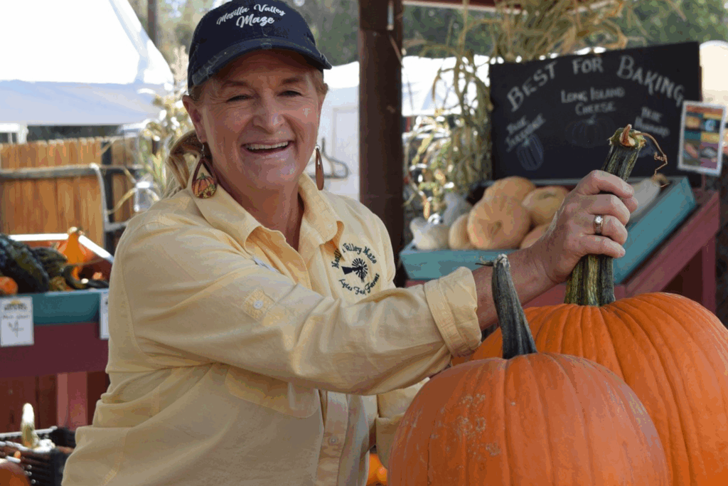 A Mesilla Valley Maze employee smiles while helping a customer with two pumpkins.