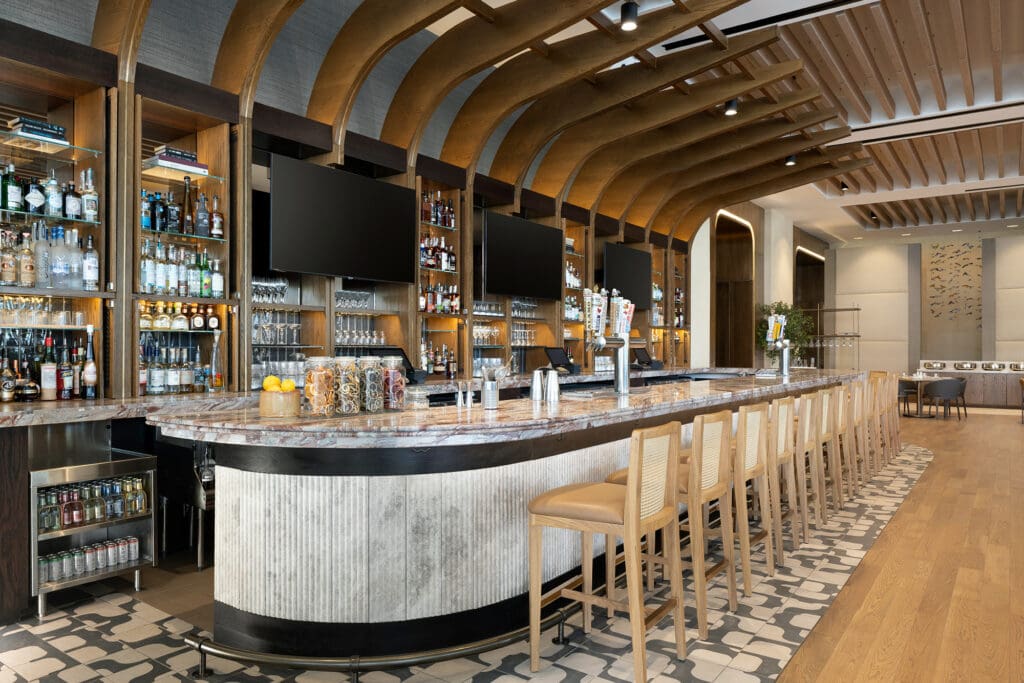 Grand Hyatt San Antonio River Walk's Bar Rojo is Moda Fare with bar seating and three TVs and multiple liquor bottles and glasses lined up on the wall.