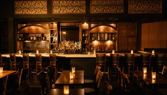 A prohibition decored bar with dark lighting and oak wood accents and seating at Nica on 4th in Downtown Austin.