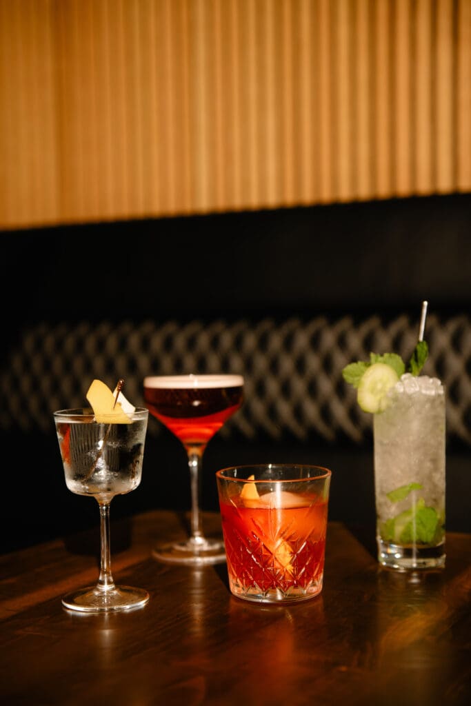 Four cocktails in different types of cocktail glasses are lined up on a table in the jazz bar, Nica on 4th in Downtown Austin.