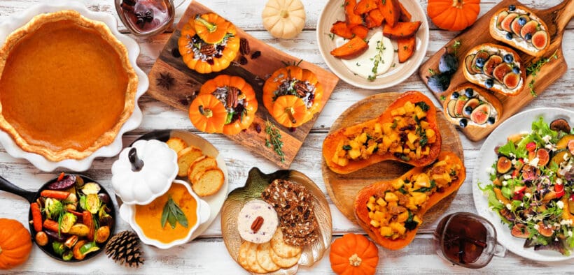 A smattering of pumpkin-themed dishes; pumpkin pie, pumpkin dip, stuffed pumpkins and squash salad on a wood table.