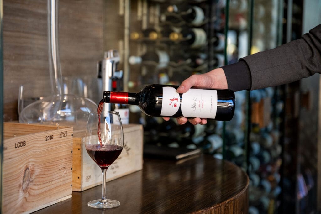 A person pours red wine into a wine glass with a wine cellar in the background at Sanctuary Camelback Mountain. 