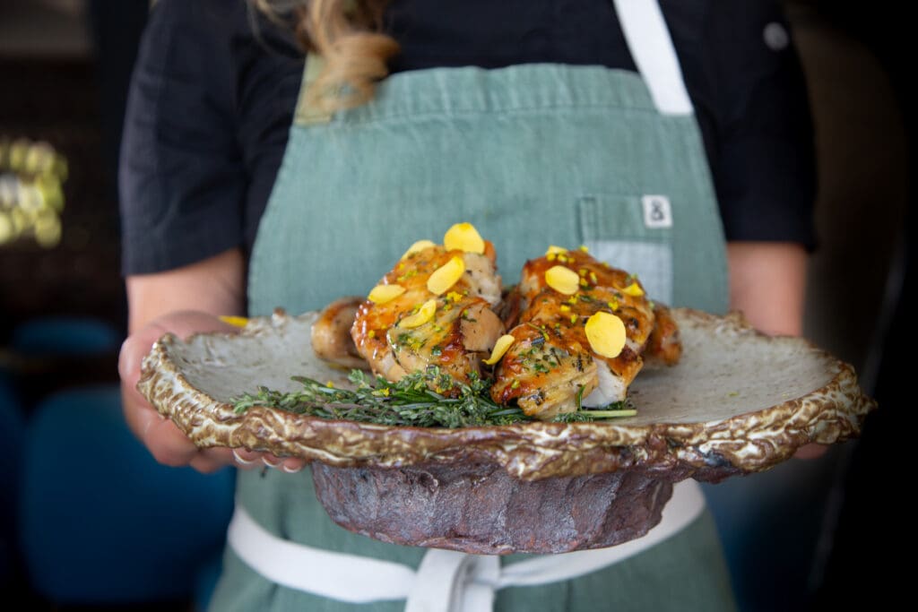 A chef holds a platter with an elegantly plated chicken and sprig of rosemary at Atria restuarnt in Flagstaff.
