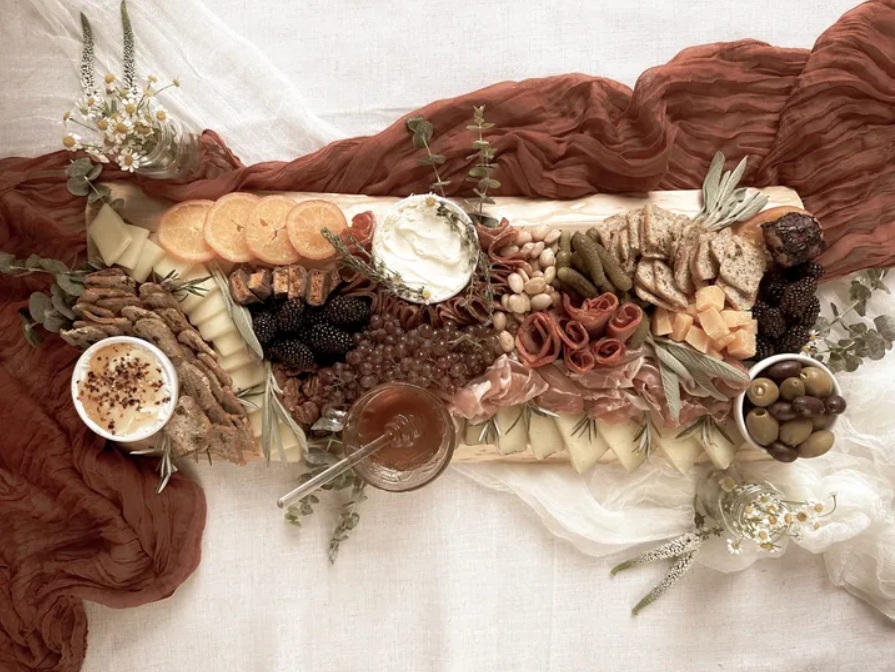Sliced oranges, meats, berries, olives and cheeses as part of a charcuterie board on top of scarves for a Fiore Della Vita event.