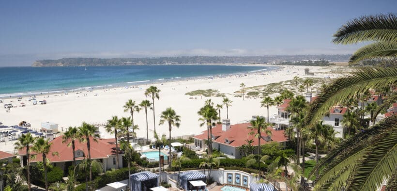 Hotel del Coronado's buildings and pool with the beach and bay of Coronado Island.