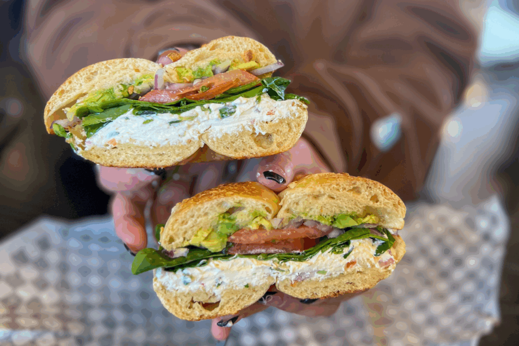 A woman holds a bagel sandwich from Fat Bagels in Flagstaff filled with lettuce, avocado, tomato and chicken salad.