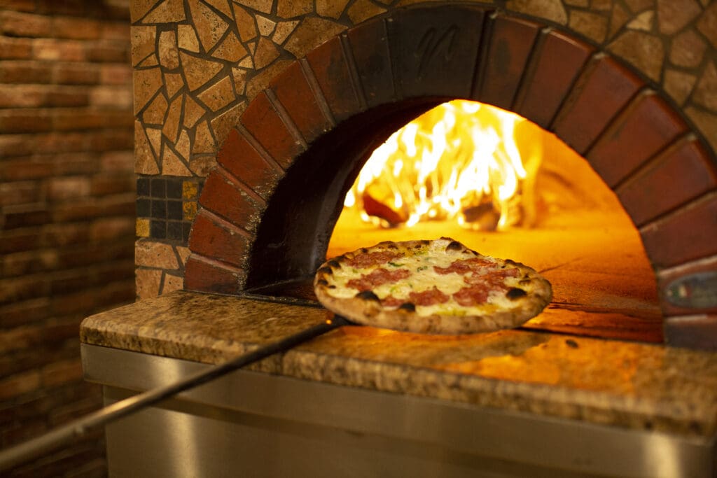 A pizza is being taken out of wood-fired, brick oven on a large metal tool at Fat Olives restaurant in Flagstaff.