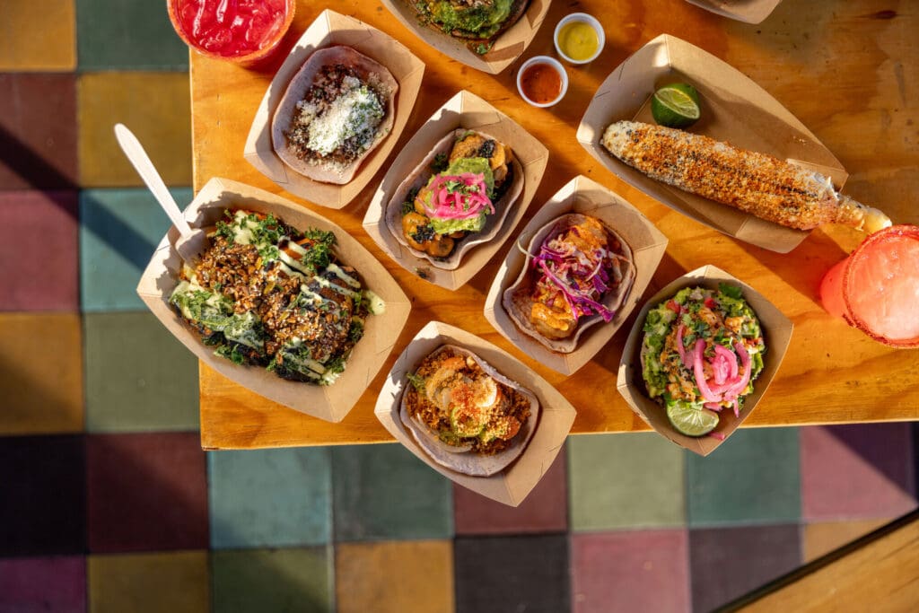 Grilled sweet potatoes, tacos, elote, salsas and drinks on a table at Taconeta in El Paso.