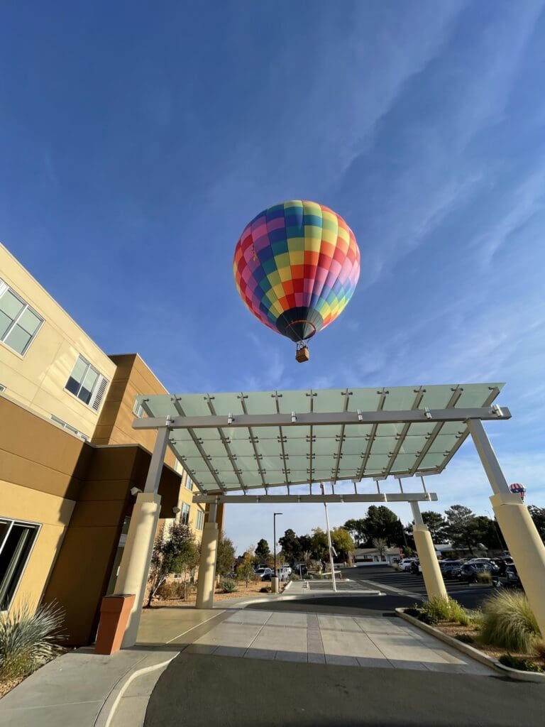 A hot air balloon hovers over the Hyatt Place Page/Lake Powell entrance with cars parked in the parking lot.