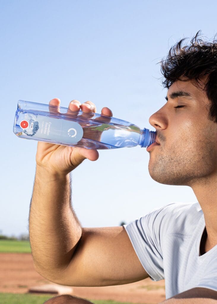 A man in workout clothes drinking a bottle of One Water Canadian Rockies spring water outside. 