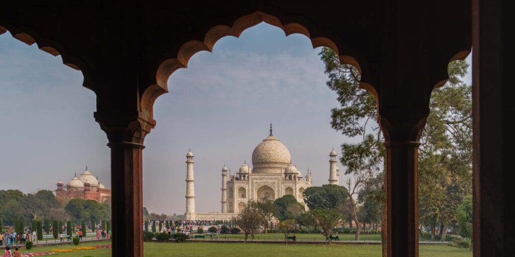 The Taj Mahal in India, with people walking around the greenery.  