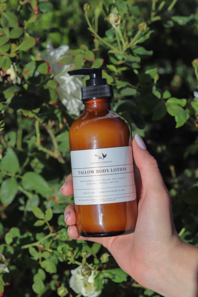 A manicured hand holds a bottle of Caldwell Cosmetics Tallow Lotion.