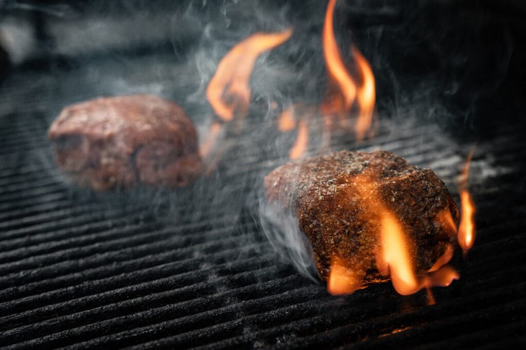 Two steaks with flames underneath on a grill at CHoP Chandler.