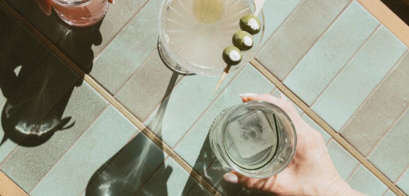 The hands of two people hold cocktails with another cocktail in the middle at Estelle restaurant in Scottsdale