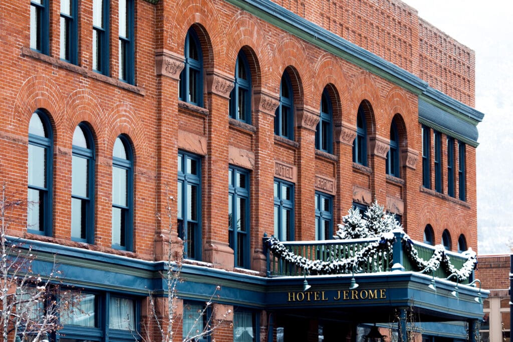 Exterior of the Hotel Jerome, Auberge Resorts Collection with snow-covered Christmas trees on a balcony.