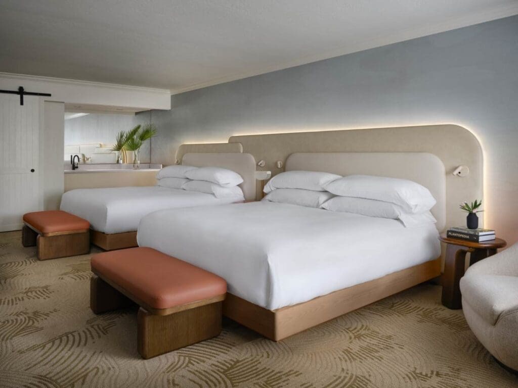 A two queen-bed guest room with footstools, bedside tables and coffee bar at Kimpton Miralina Resort & Villas in Paradise Valley, Scottsdale.