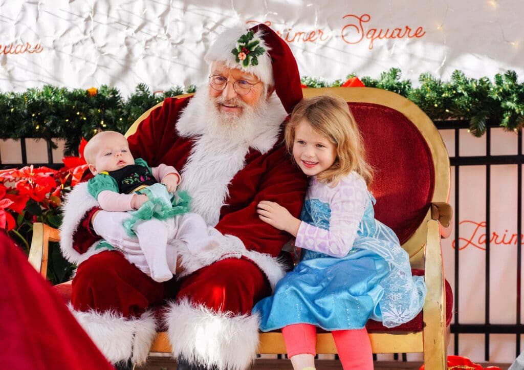 A Santa holds a baby and a girl preschooler cuddles next to Santa with holiday decor at Larimer Square in Denver. 
