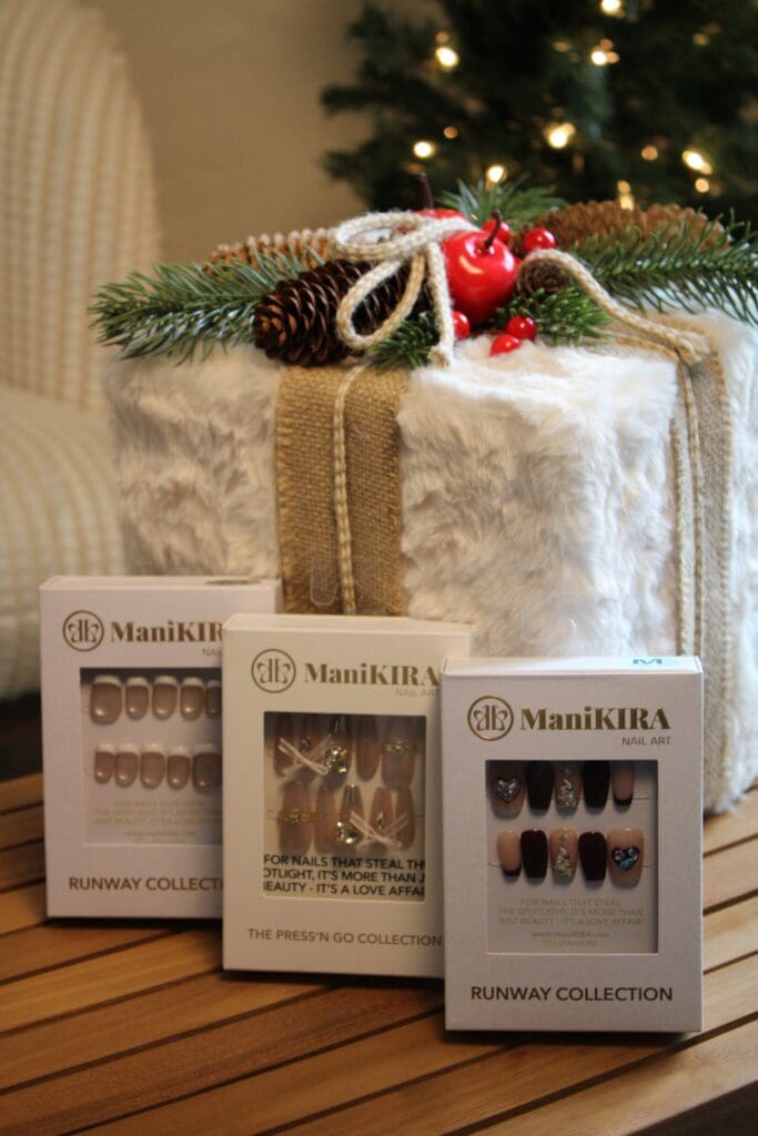 Three ManiKira press-on nail packs in front af a faux fir wrapped gift.