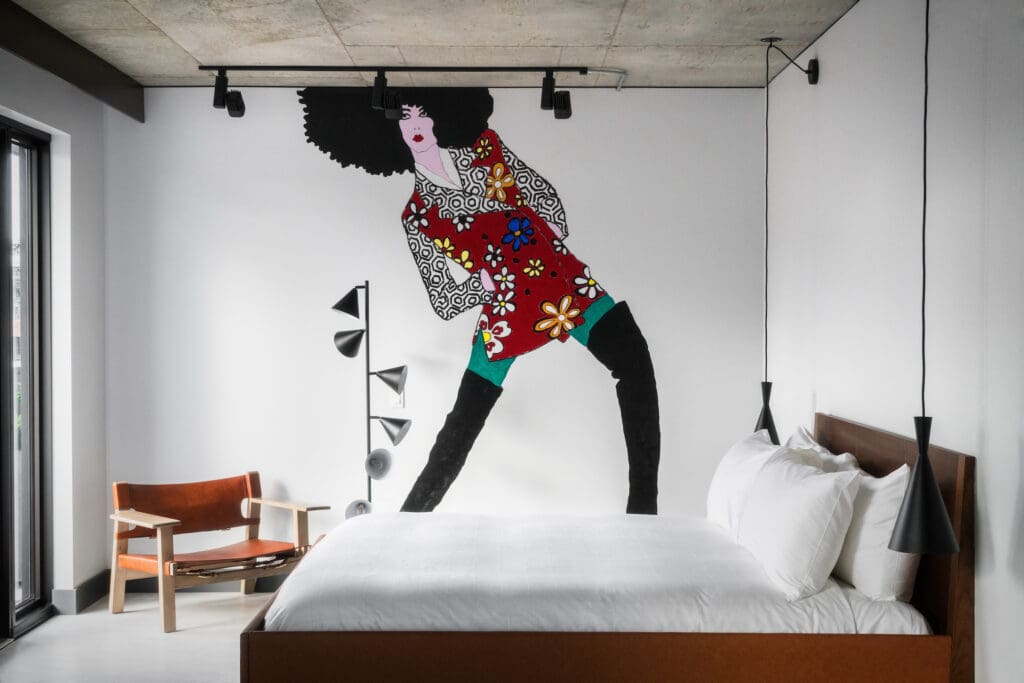 A painting of woman with an afro wearing funky on the wall of a room with a bed in The Maven Hotel in Denver. 