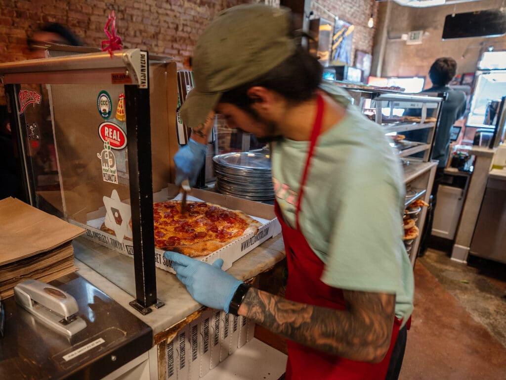 A man uses a pizza slicer to cut pieces of a pepperoni pizza at PIZZANISTA! 