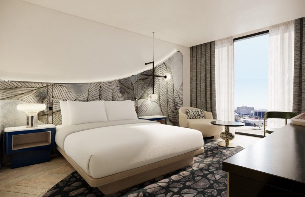 A king bed, side table, comfy chair and credenza at The Monarch San Antonio with a view of Downtown San Antonio out the window.