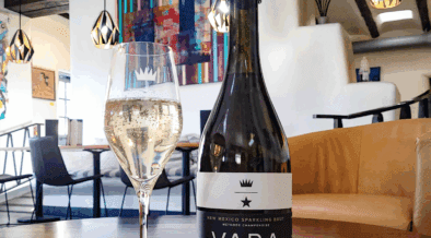 A bottle of Vara wine next to a glass of sparkling wine with the VARA Winery tasting area in the background.
