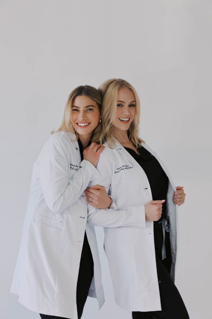 Marissa Adbo and Kendra DeMark. of Aesthetic IQ Clinic stand side by side, wearing scrubs and lab coats.