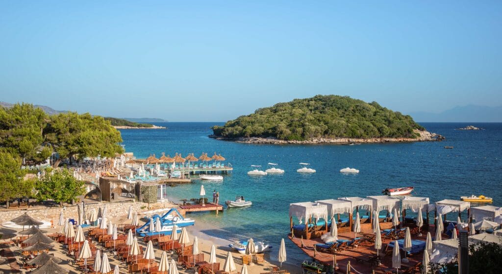 The Albanian Riviera island, beach and bay with a sandy beach, lounge chairs and umbrellas.
