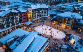 Snowmass winter base village with people on an ice-skating rink that's surrounded by lodging and holiday festivities.