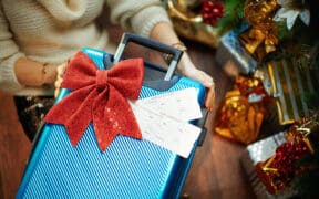 A woman receives a suitcase with two plane tickets as a gift from under the Christmas tree.