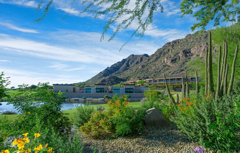 A desertscape with green hills and the The Canyon Suites at The Phoenician, a Luxury Collection Resort, with mountains in the background.