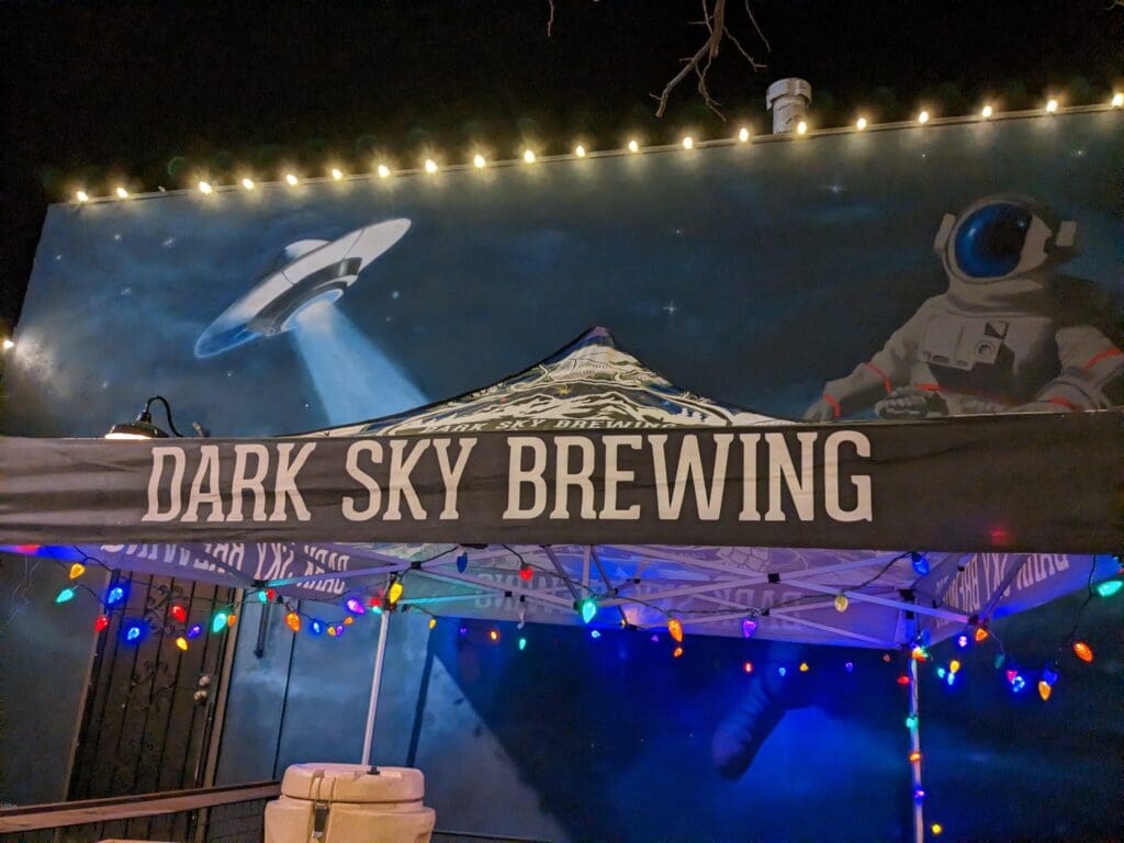 The Dark Sky Brewing Co. sign with a spaceship and astronaut above a tent and Christmas lights in Flagstaff.