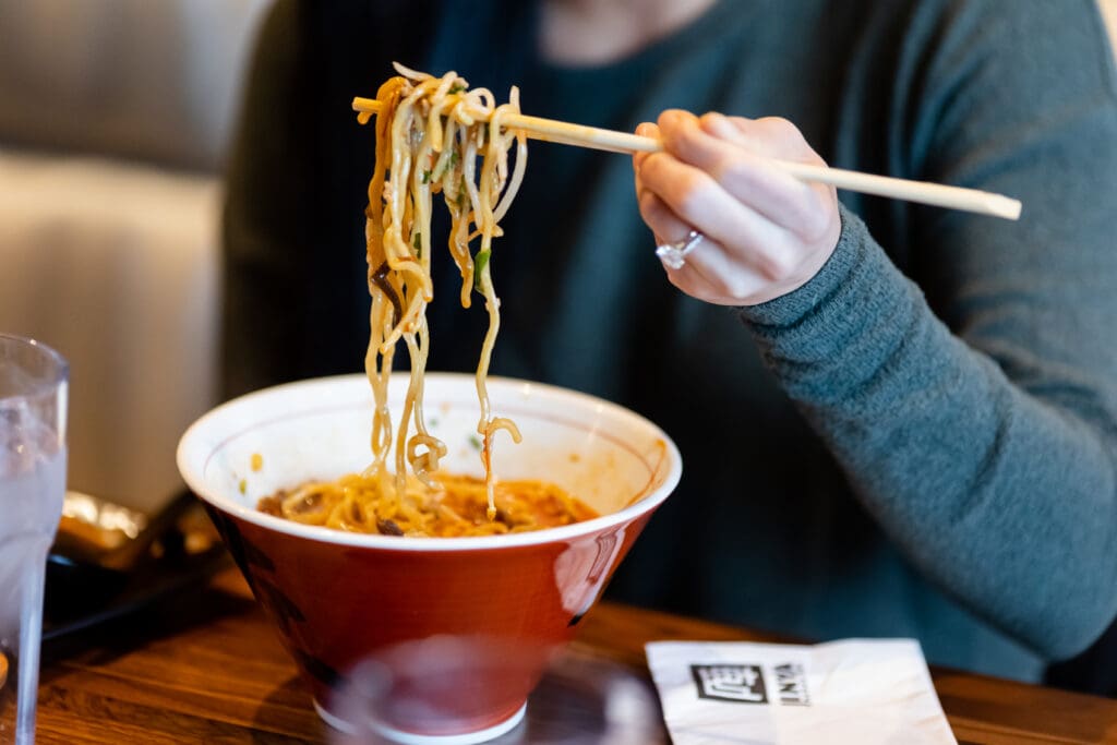 A woman holds ramen noodes in chopsticks above a bowl of ramen at JINYA Ramen Bar in Tailhead at Peoria, Arizona.
