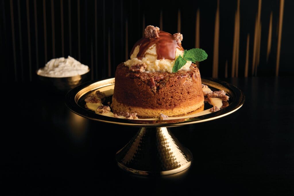 A coffee cake on a gold platter topped with ice cream and mint, garnish with a bowl of cream at Mastro's in Phoenix.