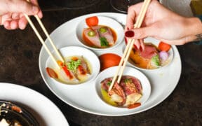 Two hands hold chopsticks, enjoying small bowls of Winter Omakase at Nobu Scottsdale.