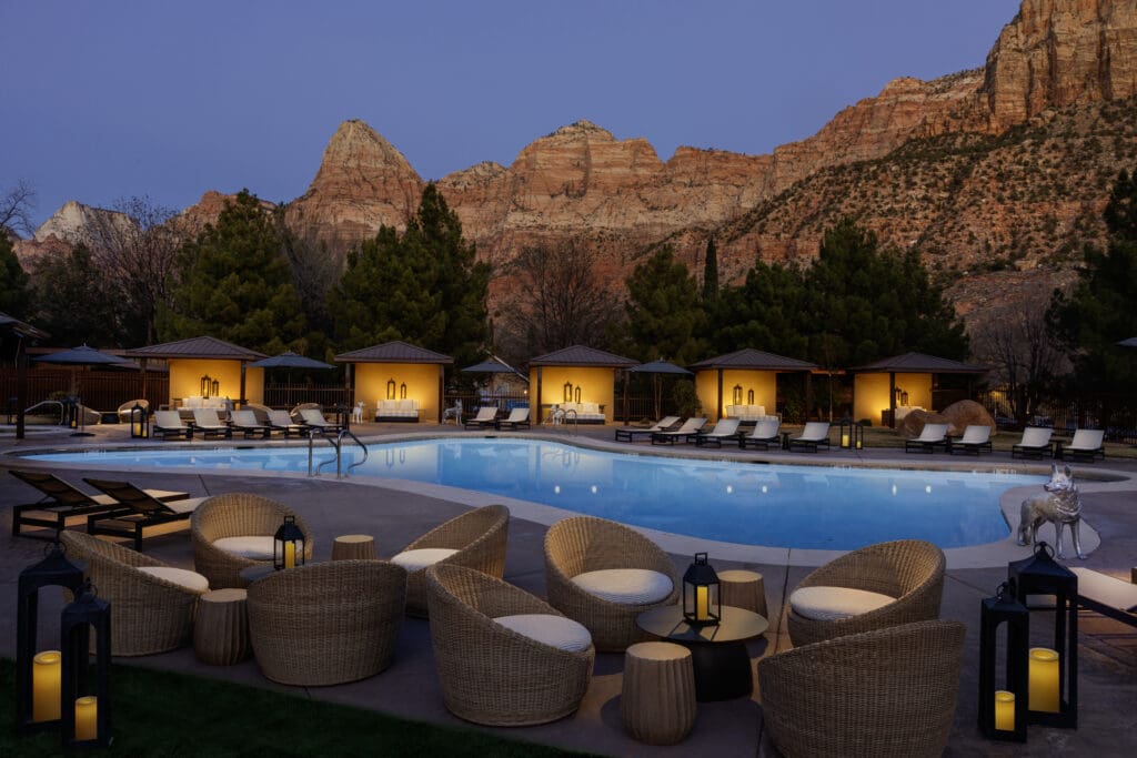 The Red Cliffs Lodge Zion pool and cabanas lit at night against the red cliffs of Zion.
