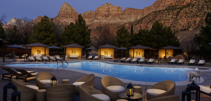 The Red Cliffs Lodge Zion pool and cabanas lit at night against the red cliffs of Zion.