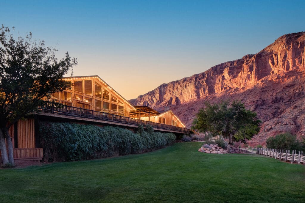 The Red Cliffs Lodge Moab with the lodge lit up in the evening next to red rock mountains.