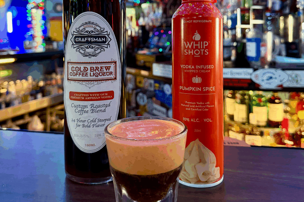 Cold Brew Coffee Liqueur bottle next to Vodka-Infused Whip Shots and a cocktail with bar in the background at Swizzle Inn, Phoenix.