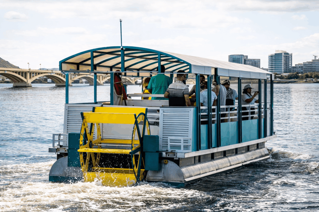The pedal boat of Tempe Boat Cruisin cruises toward the bridge and buildings of Tempe Town Lake.