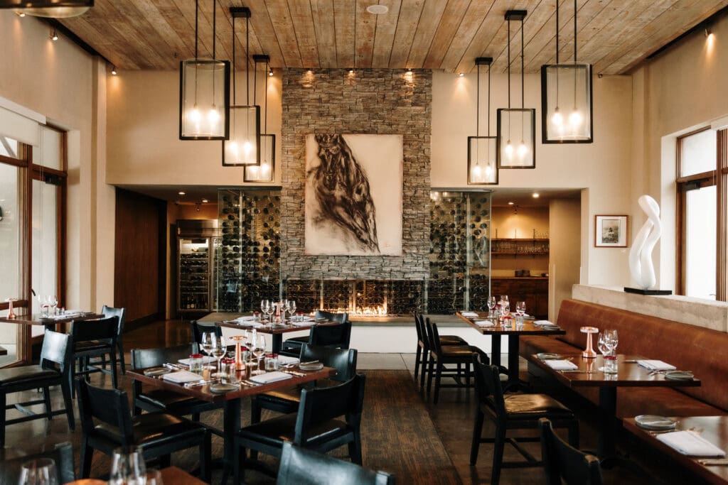 Tables with place settings and booths with a brick fireplace and wine rack at Terra at Four Seasons Resort Rancho Encantado.