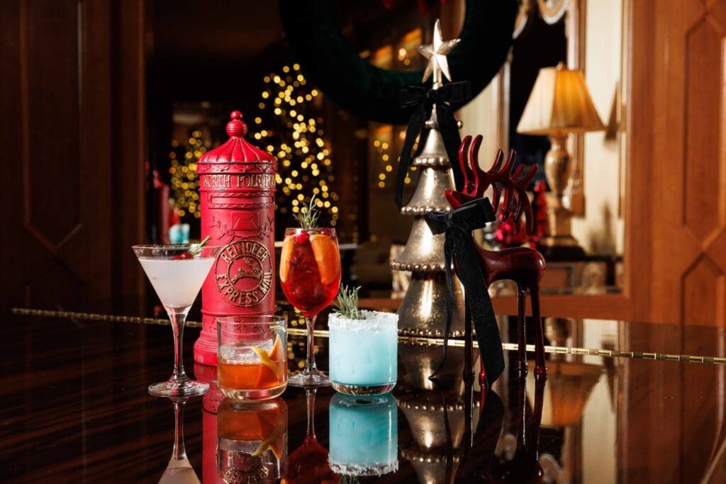 A martini glass and several cocktail glasses are lined up next to Christmas decor at The Grand America Hotel.