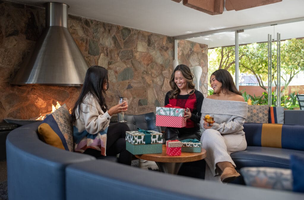 Three women share gifts at Hotel Valley Ho ZuZu with a fire in the background.