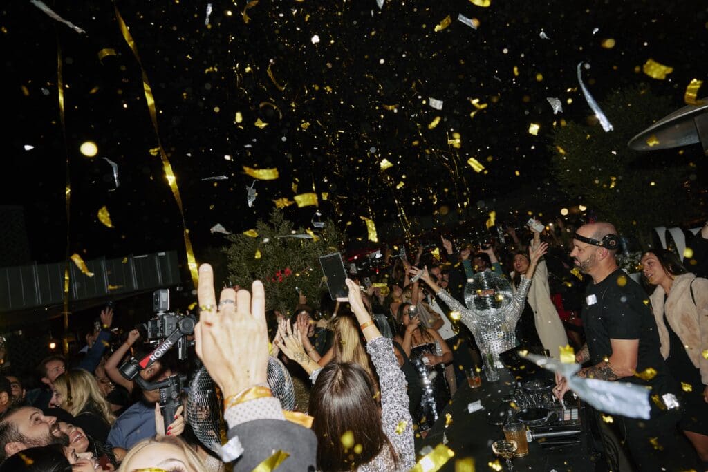 A group of people dance amid confetti while a DJ spins at théa rooftop restaurant at The Global Ambassador.
