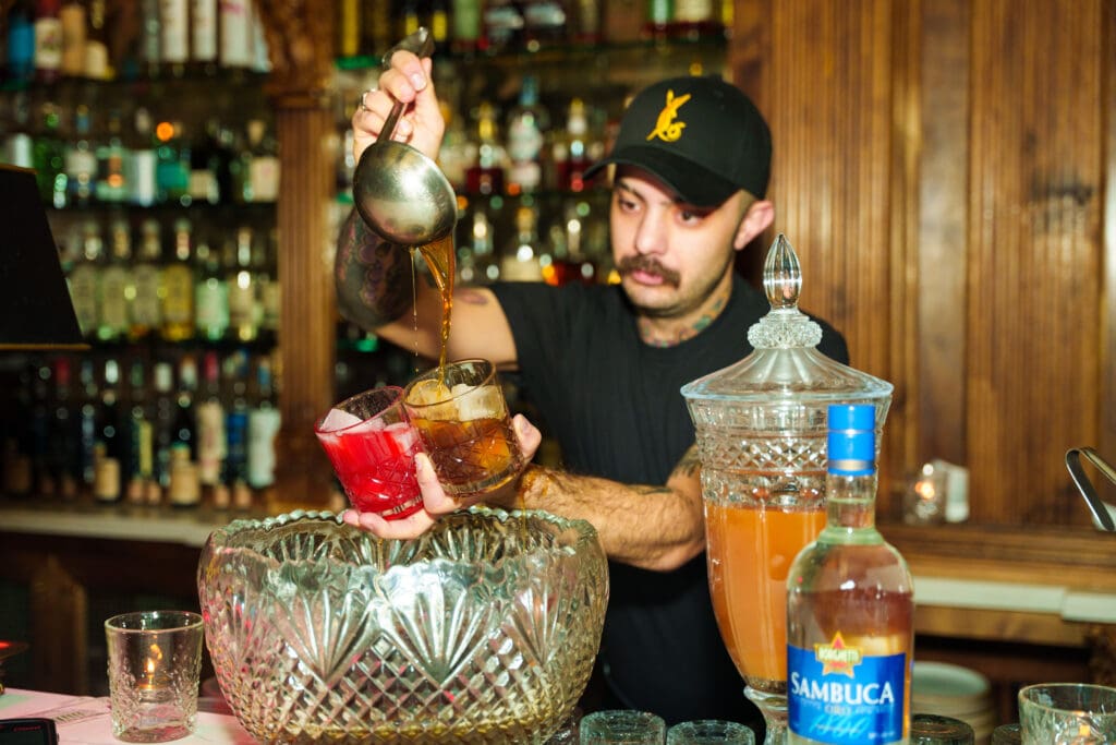 A bartender pours liquor into cocktail glasses over a glass punch bowl for Arizona Cocktail Weekend.