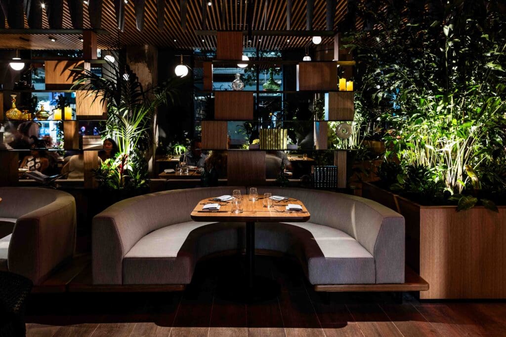 A booth with a set table, several plants and modern decor with low lighting at BOA Steakhouse.