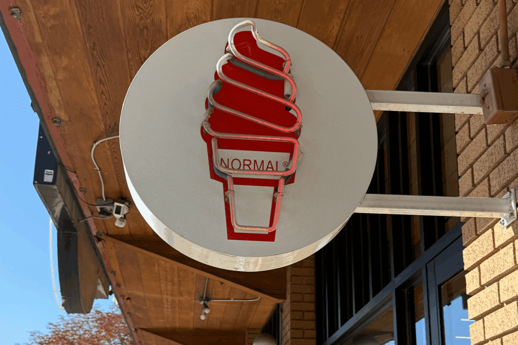 An unlit neon sign of a soft serve ice cream with text "Normal" on the storefront of Normal ice cream in Maven District, Salt Lake City.