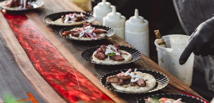 A row of plated tacos with meet and veggies with various squeeze sauces and a person pointing to them at Taste of AZ in Scottsdale.